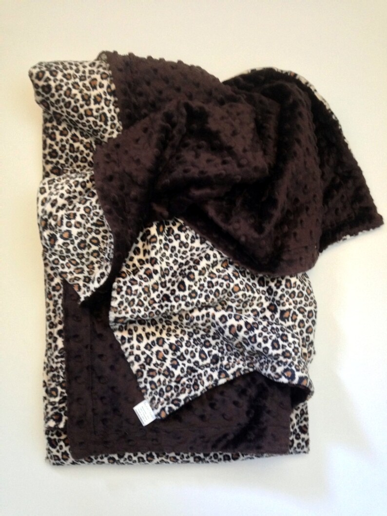 May include: A brown and leopard print fleece blanket. The blanket is folded in half and has a soft, fuzzy texture.