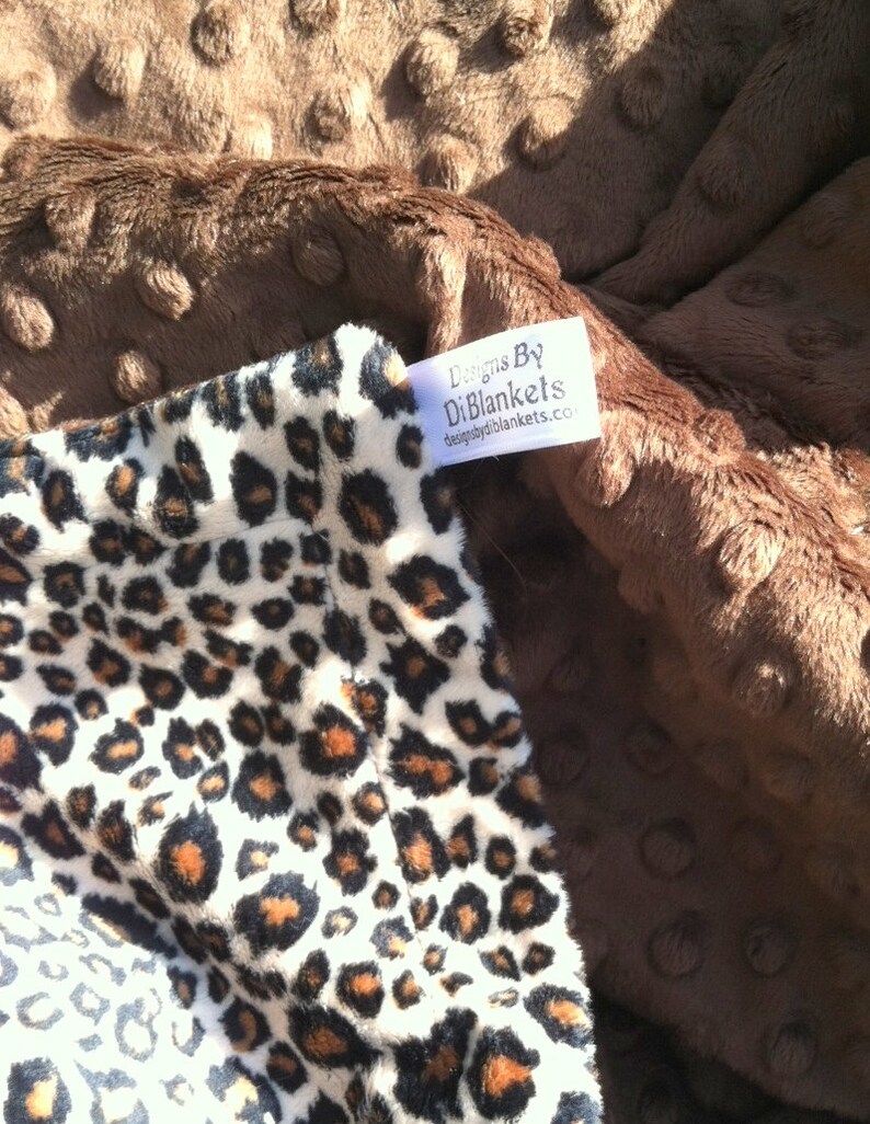 May include: A brown minky dot fabric blanket with a white and brown leopard print fabric on one side. The blanket has a white tag that says "Designs By DiBlankets thedesignsbydiblankets.com".
