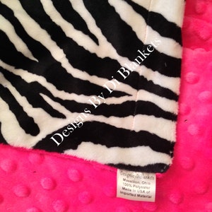 May include: A pink and black zebra print baby blanket with a minky dot fabric on the back. The blanket has a tag that reads "Designs By Di Blankets Massillon, Ohio 100% Polyester Made in USA of Imported Material."