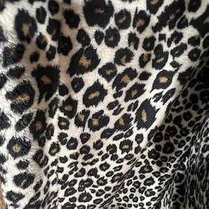 May include: Close-up of a white fabric with a black and brown leopard print pattern. The fabric is soft and plush, with a fuzzy texture.