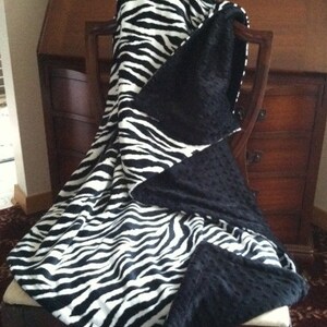 May include: A black and white zebra print throw blanket with a black minky backing. The blanket is draped over a chair.