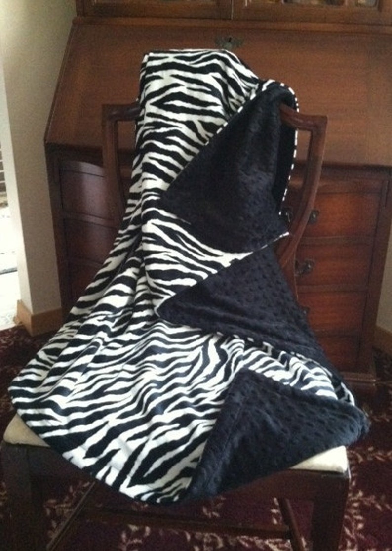 May include: A black and white zebra print throw blanket with a black minky backing. The blanket is draped over a chair.
