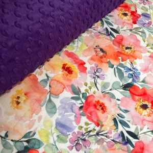 May include: A purple plush fabric with a textured surface is placed on top of a white fabric with a watercolor floral print. The floral print features pink, orange, and yellow flowers with green leaves.