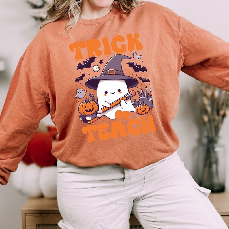 May include: Orange sweatshirt with a ghost wearing a witch hat and holding a pencil. The text "Trick or Teach" is printed on the sweatshirt.