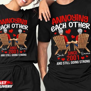 May include: A black t-shirt featuring a graphic of two people with gray hair sitting in wooden chairs, holding hands. The text reads ANNOYING EACH OTHER, SINCE 2001, AND STILL GOING STRONG, with the names Jack and Emma printed below the chairs.