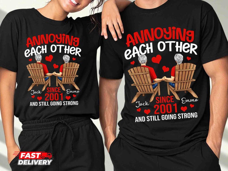 May include: A black t-shirt featuring a graphic of two people with gray hair sitting in wooden chairs, holding hands. The text reads ANNOYING EACH OTHER, SINCE 2001, AND STILL GOING STRONG, with the names Jack and Emma printed below the chairs.