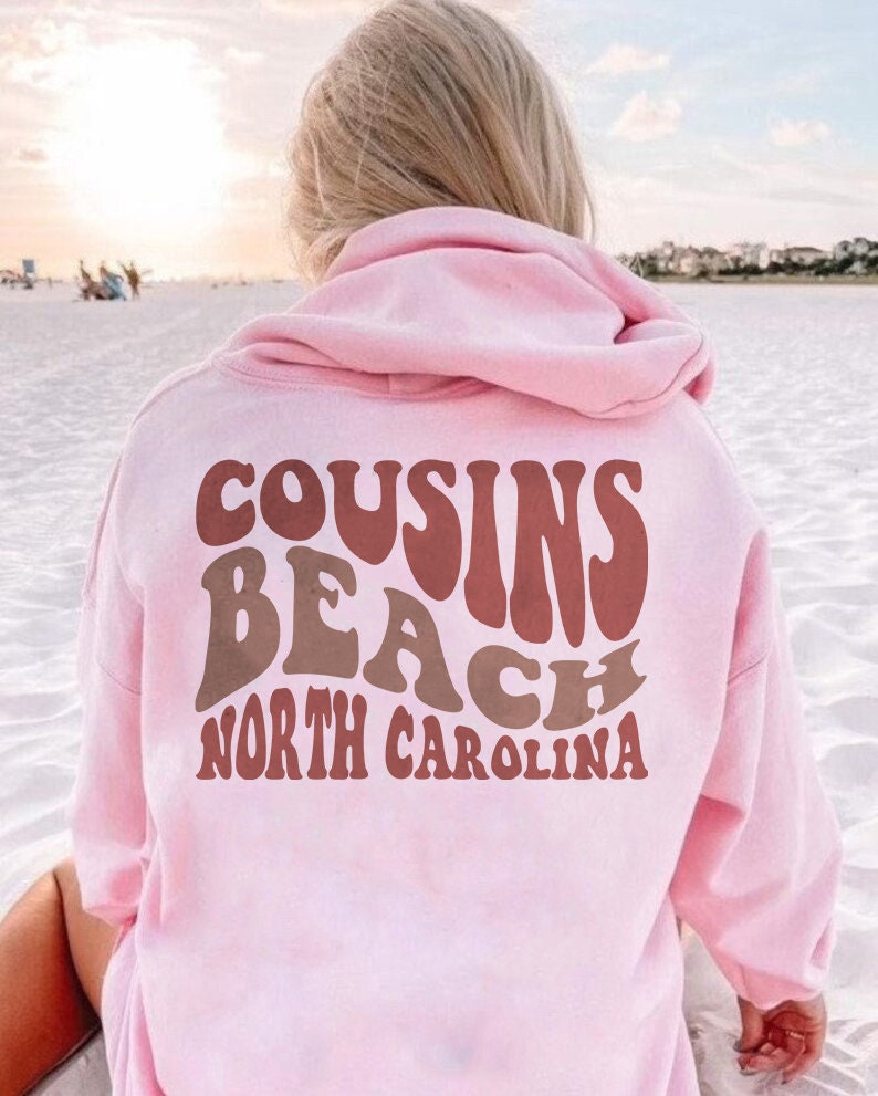 May include: Pink hooded sweatshirt with the text "COUSINS BEACH NORTH CAROLINA" in a retro font.