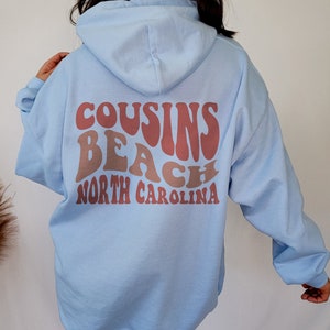 May include: A light blue hooded sweatshirt with the text "COUSINS BEACH NORTH CAROLINA" in a retro font printed on the back.
