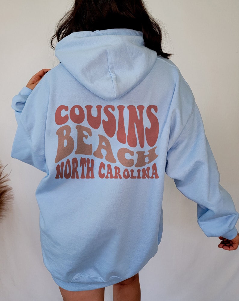 May include: A light blue hooded sweatshirt with the text "COUSINS BEACH NORTH CAROLINA" in a retro font printed on the back.