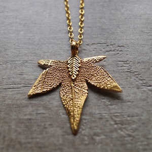 May include: A gold necklace with a detailed leaf pendant. The leaf is made of metal and has a delicate, intricate design.