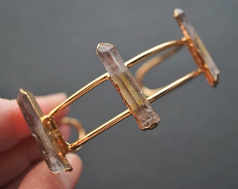 May include: Gold bangle bracelet with three clear quartz crystals attached. The crystals are raw and have a natural, irregular shape.