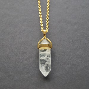 Peut inclure: Un collier en chaîne dorée avec un pendentif en cristal de quartz transparent. Le cristal est en forme de pointe et est serti dans une bélière dorée.