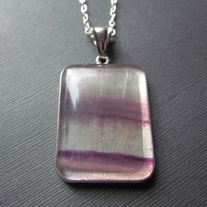 May include: A silver chain necklace with a rectangular pendant featuring a purple and white fluorite stone.