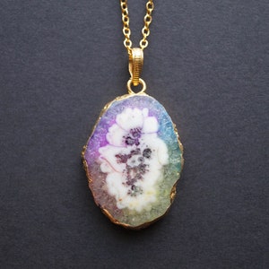Peut inclure: Un collier en cha&icirc;ne dor&eacute;e avec un pendentif en forme de tranche d'agate color&eacute;e avec un motif de fleur blanche.