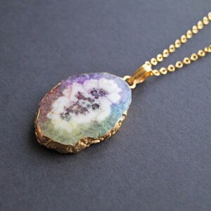Peut inclure: Un collier en cha&icirc;ne dor&eacute;e avec un pendentif en forme de tranche d'agate aux couleurs arc-en-ciel et un motif de fleur blanche.