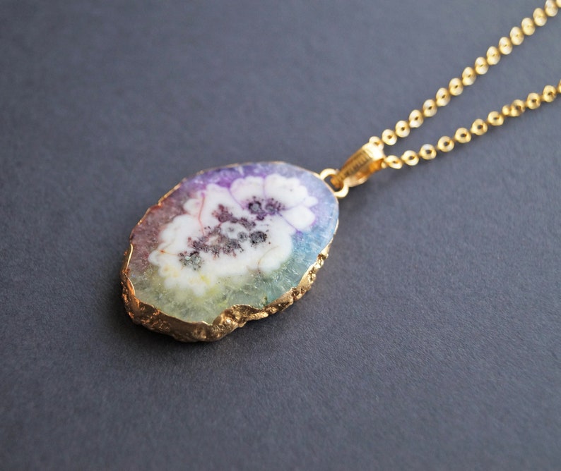 Peut inclure: Un collier en cha&icirc;ne dor&eacute;e avec un pendentif en forme de tranche d'agate aux couleurs arc-en-ciel et un motif de fleur blanche.