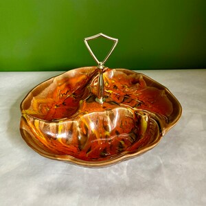 Puede incluir: Un plato de servir de cerámica marrón y naranja con tres secciones y un asa de metal. El plato tiene un patrón de espiral y un acabado brillante.