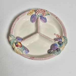 Könnte beinhalten: Eine weiße Keramik-Servierplatte mit drei Abschnitten. Die Platte ist mit einem rosa Seilrand und einem bunten Fruchtdesign verziert, das Pflaumen, Beeren und Blätter zeigt.