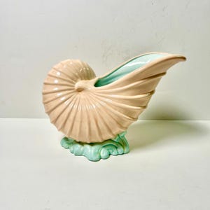 Peut inclure: Vase en céramique en forme de coquillage nautile, pêche clair avec intérieur et base turquoise. Le design de la coquille présente des arêtes et des courbes détaillées, créant une pièce décorative unique.