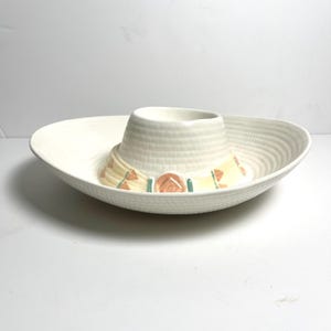 以下が含まれることがあります： 白いセラミック製のソンブレロ型チップ＆ディップサービング皿。ソンブレロは、テクスチャード加工されたつばと中央のディップボウルを備えています。帽子バンドは、オレンジ、黄色、緑のアクセントで装飾されています。この皿は、スナックの提供用に設計されています。