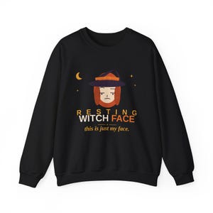 May include: A black long-sleeve sweatshirt featuring a graphic of a person wearing a witch hat. The text reads RESTING WITCH FACE and this is just my face. The design includes a small crescent moon and stars in orange and purple tones.