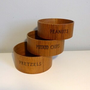 May include: Three wooden bowls stacked on top of each other. The bottom bowl says "Pretzels", the middle bowl says "Potato Chips", and the top bowl says "Peanuts".