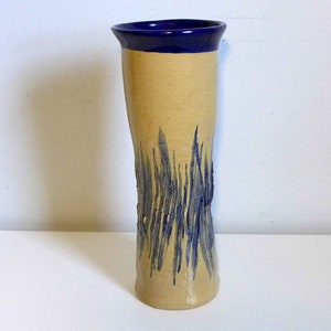 May include: A tall, ceramic vase with a light brown body and a blue rim. The vase has a blue and white abstract design on the front.