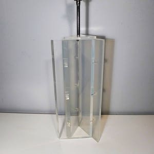 May include: A clear acrylic lamp base with a geometric design. The base is made of multiple panels that are joined together. The lamp base is empty and ready to be used with a lampshade.