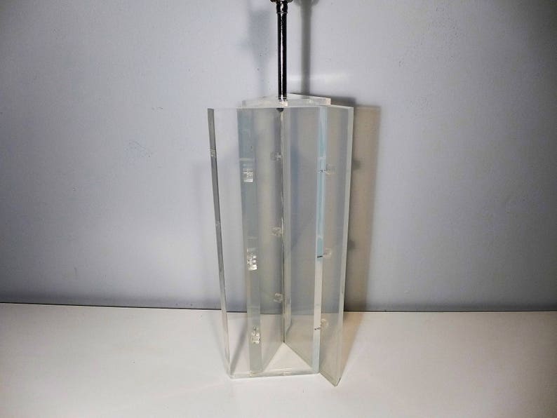 May include: A clear acrylic lamp base with a geometric design. The base is made of multiple panels that are joined together. The lamp base is empty and ready to be used with a lampshade.