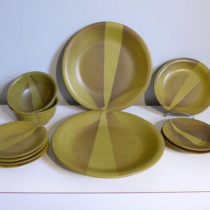 May include: A set of green and brown ceramic dinnerware with a geometric pattern. The set includes a large dinner plate, a smaller salad plate, and a bowl.