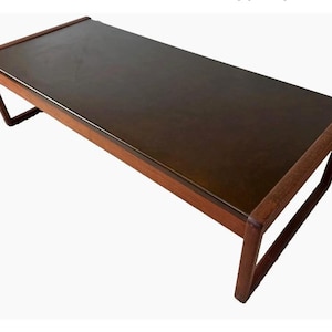May include: A rectangular coffee table with a dark brown top and a wooden frame. The legs are angled, and the table has a mid-century modern design. The table is approximately 48 inches long.
