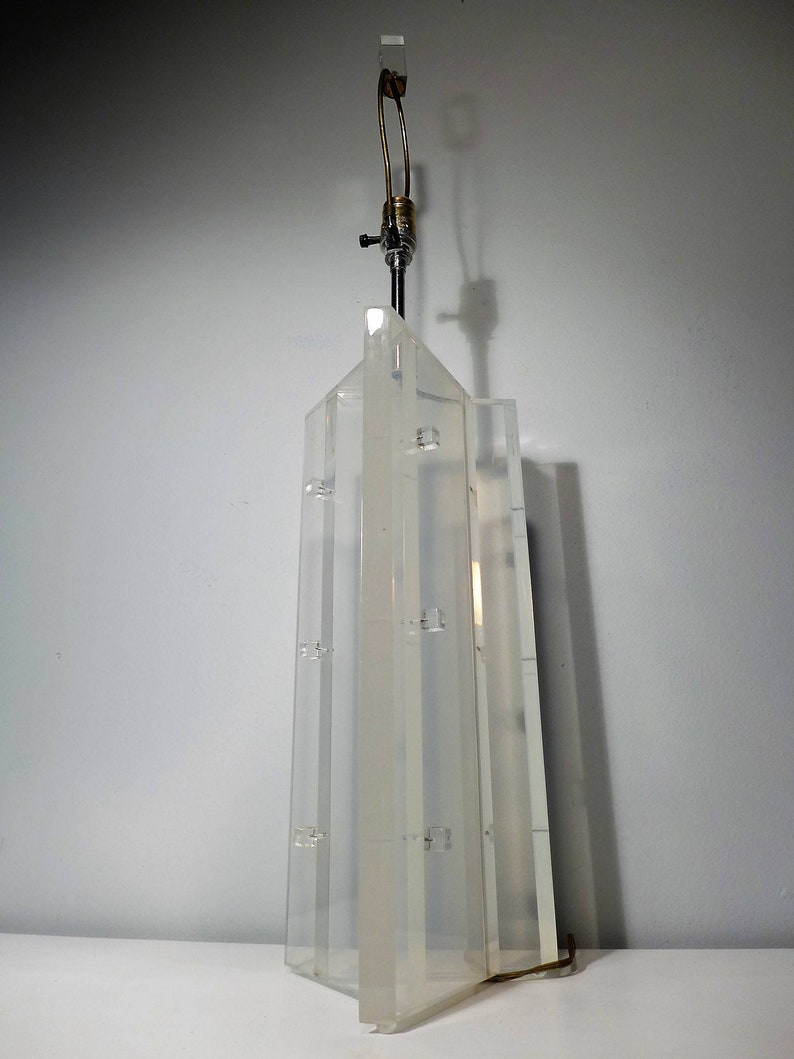 May include: A clear acrylic table lamp with a geometric design. The lamp has a metal base and a clear glass shade.