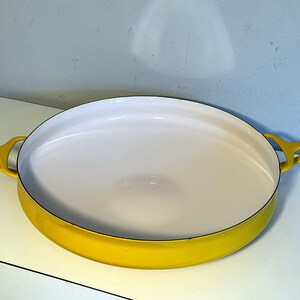 May include: A yellow oval-shaped enamel baking dish with white interior and two black handles.