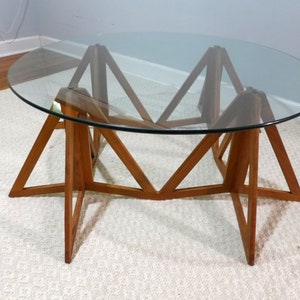 May include: A round glass top coffee table with a unique wooden base. The base is made of six triangular pieces of wood that are joined together to form a star shape.