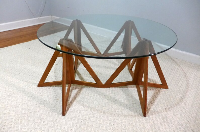 May include: A round glass top coffee table with a unique wooden base. The base is made of six triangular pieces of wood that are joined together to form a star shape.
