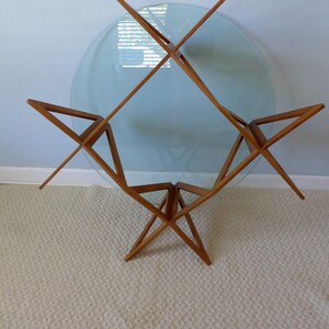 May include: A mid-century modern glass and wood coffee table with a circular glass top and a starburst-shaped base.