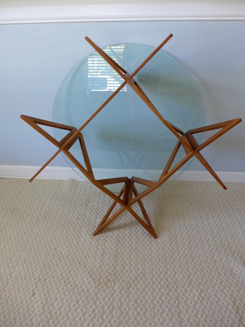 May include: A mid-century modern glass and wood coffee table with a circular glass top and a starburst-shaped base.