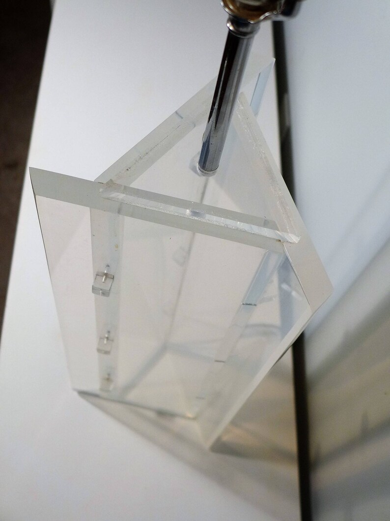 May include: A clear acrylic prism with a metal rod inserted through the top. The prism is made of multiple pieces of acrylic that are joined together. The prism is sitting on a white surface.