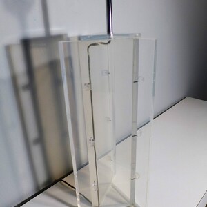 May include: A clear acrylic table lamp with a chrome base and a silver cord.