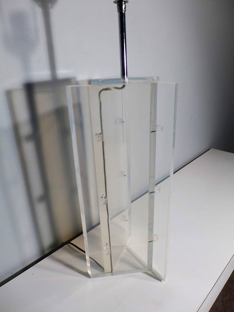 May include: A clear acrylic table lamp with a chrome base and a silver cord.