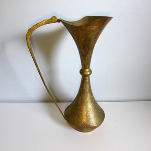May include: A gold-colored brass vase with an ornate design and a curved handle. The vase has a wide mouth and a narrow base.
