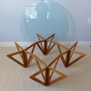 May include: A mid-century modern coffee table with a round glass top and a geometric wooden base. The base is made of four sets of triangular pieces that intersect to form a star shape.