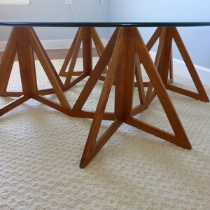 May include: A round glass top coffee table with a unique wooden base made of triangular shapes. The base is made of light brown wood and has a geometric design.