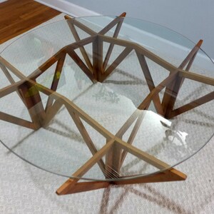 May include: A round glass-top coffee table with a unique geometric wooden base. The base is made of multiple pieces of wood that are joined together to create a starburst pattern.