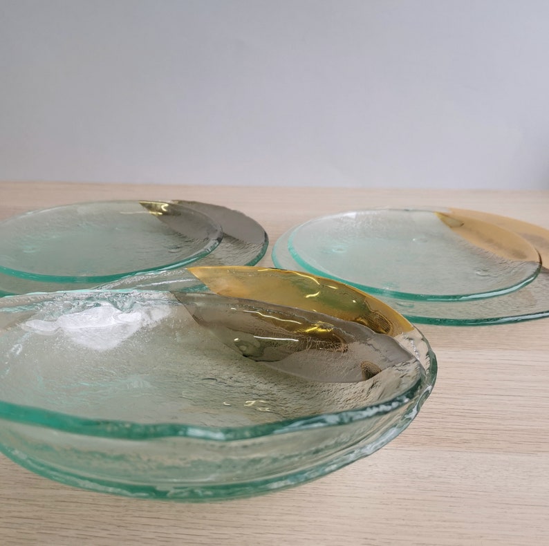 May include: Three glass plates with a textured surface and a gold rim. The plates are stacked on top of each other.