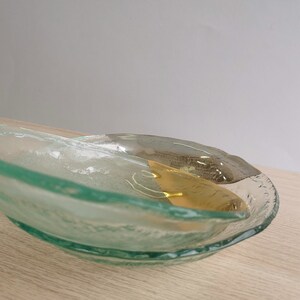 May include: A clear glass serving dish with a wavy edge and a gold accent. The dish is made of textured glass and has a unique, organic shape.