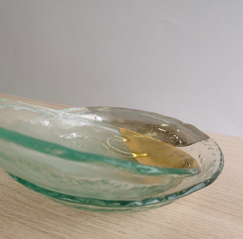 May include: A clear glass serving dish with a wavy edge and a gold accent. The dish is made of textured glass and has a unique, organic shape.