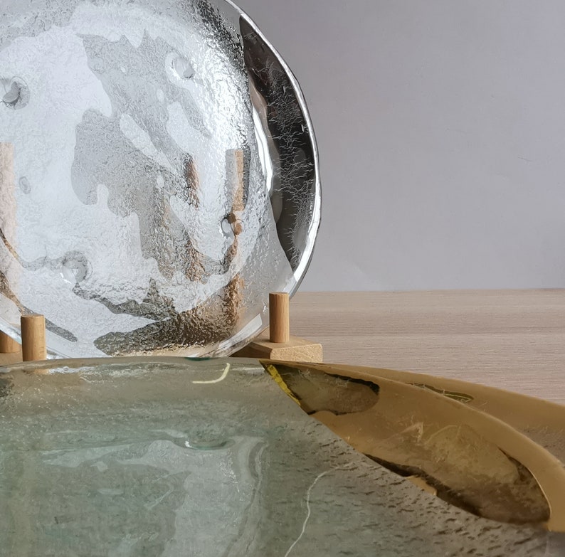 May include: Two glass plates, one clear and one with a frosted, textured surface, are displayed on a wooden stand. The clear plate is on top of the frosted plate.
