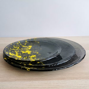 May include: Three black ceramic plates, one with a yellow splatter design, stacked on top of each other.