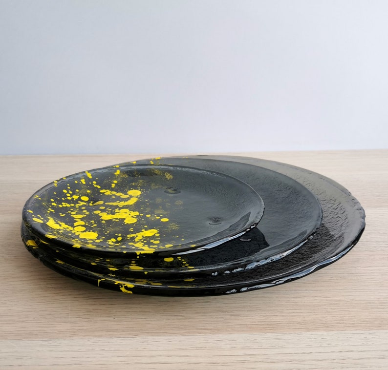 May include: Three black ceramic plates, one with a yellow splatter design, stacked on top of each other.